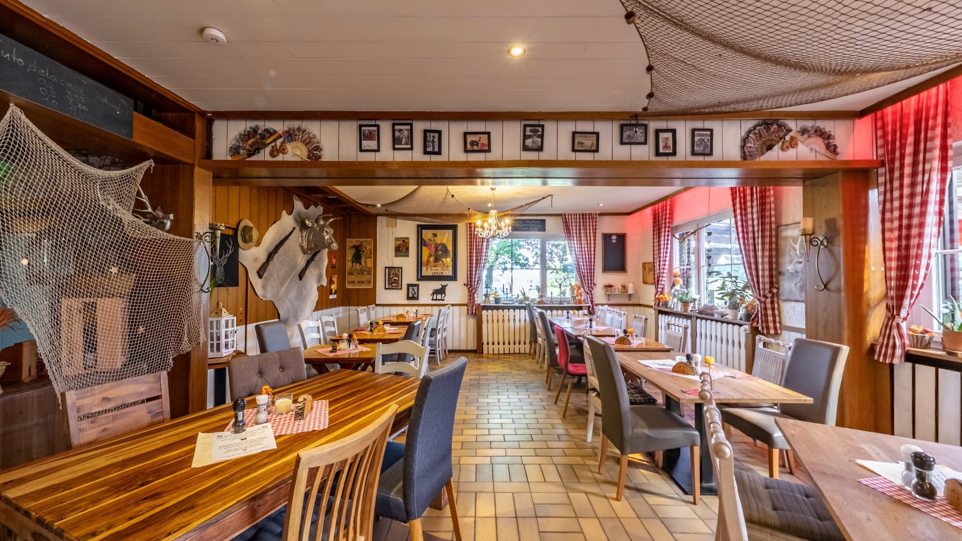 Gemütlich eingerichtetes Restaurant mit Holztischen, gemischten Stühlen, roten Karovorhängen und Wanddekoration im rustikalen Stil